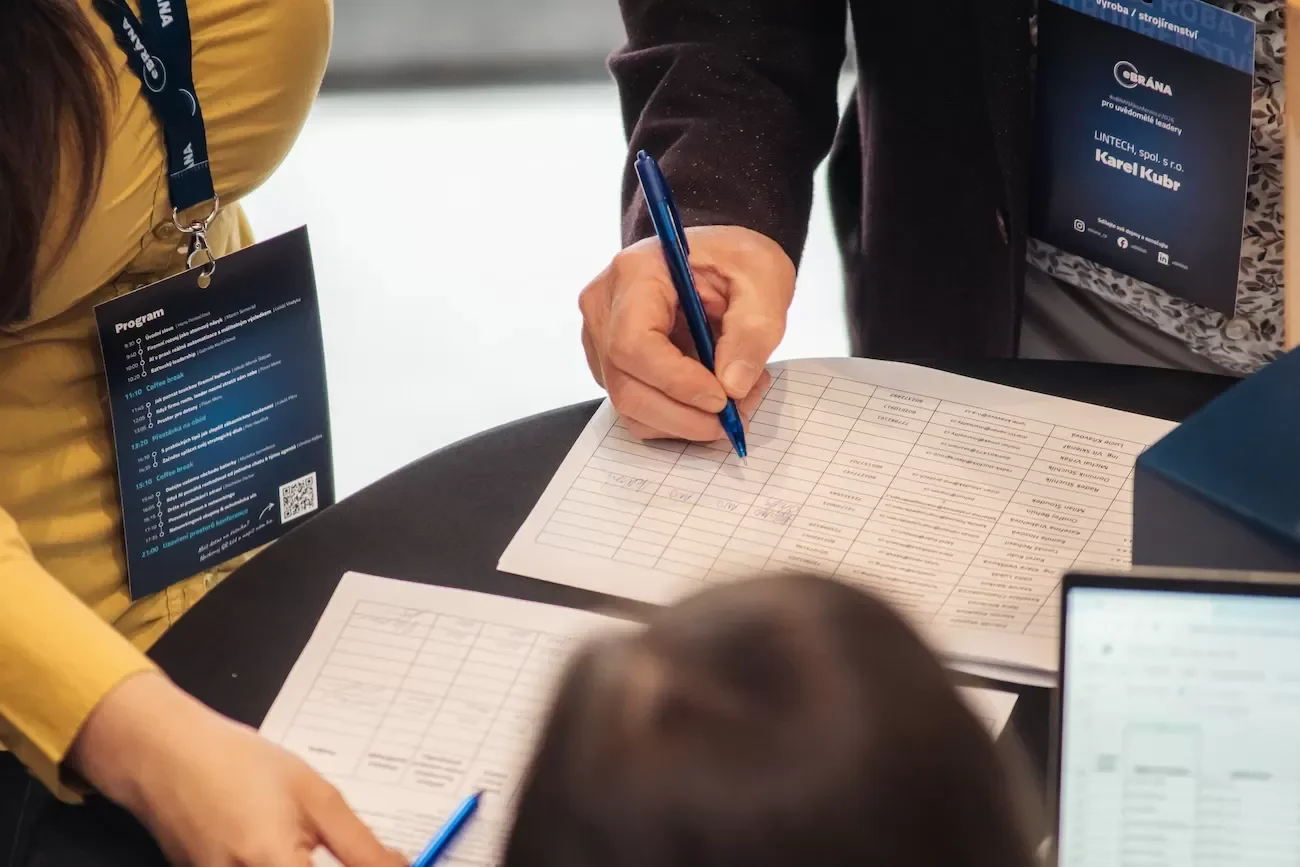 Detail ruky s propiskou zapisující se na prezenční listinu workshopů.