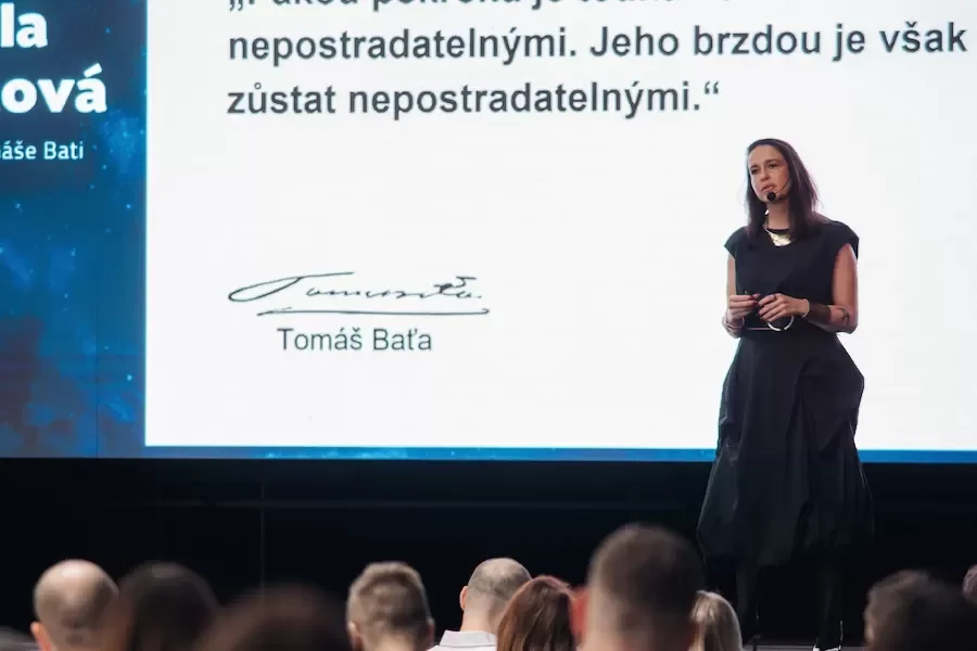 Přednášející mluví na pódiu před velkou obrazovkou.